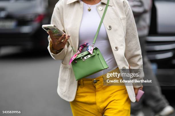 Guest wears gold necklaces, a white t-shirt, a white latte jacket from Loewe, a green matte leather mini Kelly crossbody bag from Hermes, a pale pink...