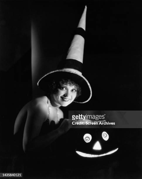Clara Bow enigmatic portrait wearing witches hat as she holds lit Halloween pumpkin for publicity photo circa 1928.
