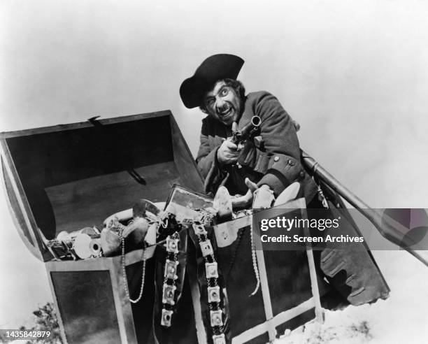 Robert Newton pointing gun by treasure chest as the infamous pirate from the 1954 movie Long John Silver's Return to Treasure Island.