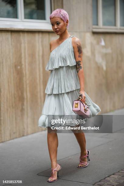 Guest wears pale green earrings, a pale blue pleated / accordion / asymmetric shoulder ruffled short dress, a pale pink matte leather with a gold...