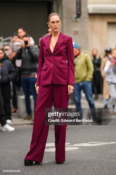 Guest wears brown sunglasses, a burgundy blazer jacket, matching burgundy suit flared pants, a gold bracelet, gold rings, black shiny leather...