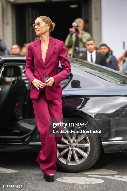 Guest wears brown sunglasses, a burgundy blazer jacket, matching burgundy suit flared pants, a gold bracelet, gold rings, black shiny leather...