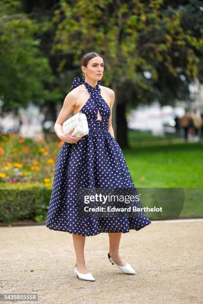 Guest wears gold earrings, a navy blue with white polka dots print pattern halter-neck / cut-out chest / midi dress, a white matte leather clutch...