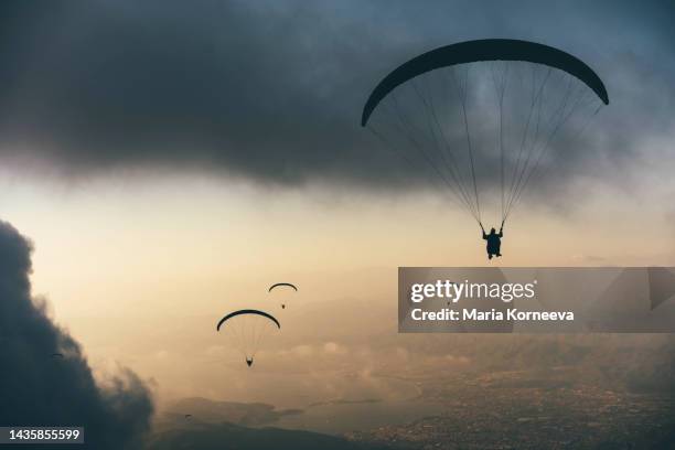 silhouette of people flying on a paraglider against the sky during sunset. - außergewöhnliche sportarten stock-fotos und bilder