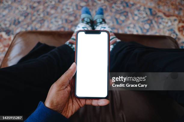 woman holds smart phone with blank screen while resting feet on ottoman - tomada fotografías e imágenes de stock