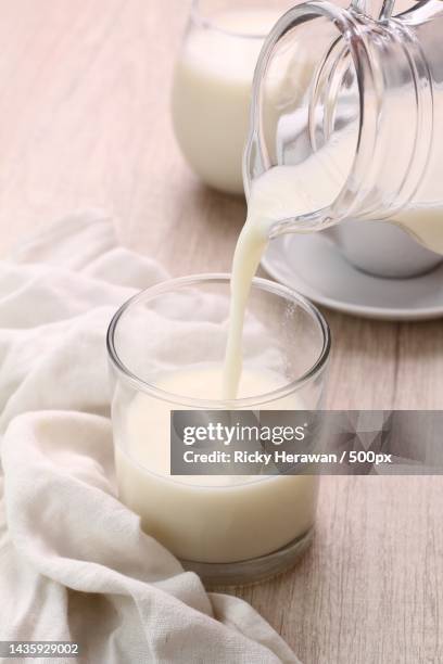 high angle view of milk pouring milk in glass on table - dairy product stock-fotos und bilder