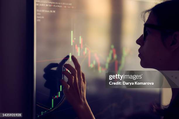 a young woman in shadow looks at the investment schedule. a woman with glasses decides where to invest money, touches the screen, the concept of saving and multiplying money. with copy space. - large scale screen stock-fotos und bilder