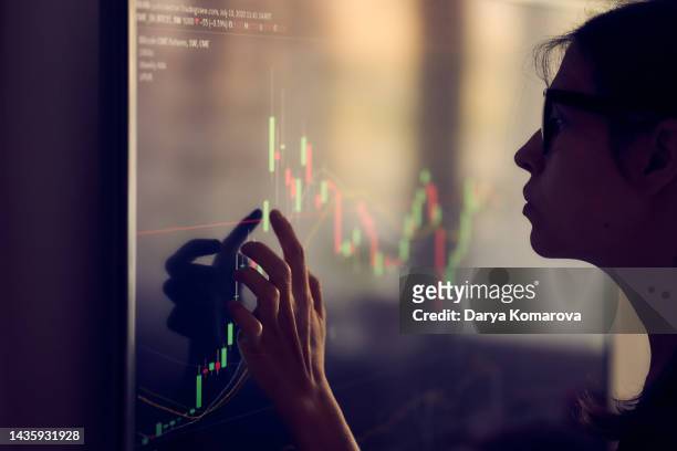 a young woman in shadow looks at the investment schedule. a woman with glasses decides where to invest money, touches the screen, the concept of saving and multiplying money. with copy space. - investors ストックフォトと画像