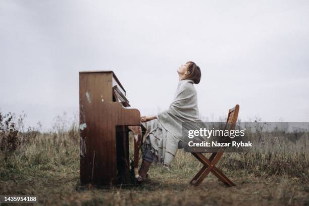 a beautiful woman is playing the piano with pleasure in a field in autumn - piano concert stock pictures, royalty-free photos & images