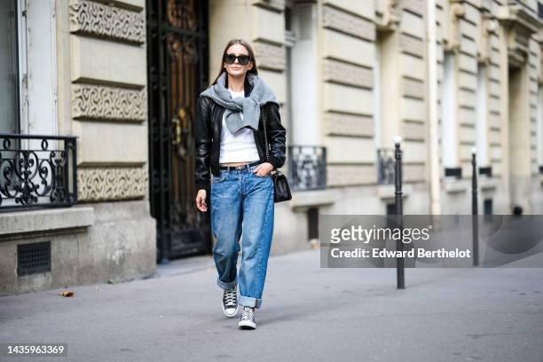 Diane Batoukina wears blue denim jeans / pants with hems from Anine Bing, a white t-shirt from Anine Bing, a black leather jacket from IKKS, a gray...