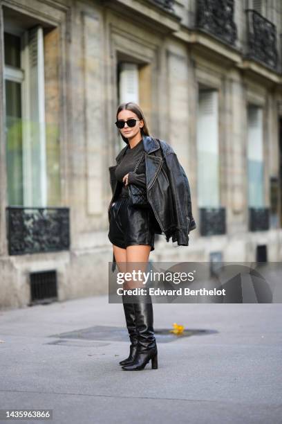 Diane Batoukina wears a black oversized leather jacket from Zara, black leather shorts from LPA, a brown cashmere sweater from Zara, knee-high...