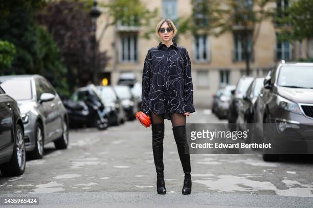 Emy Venturini wears sunglasses, a black and white shirt dress with printed patterns from Balenciaga, black thigh high pointed high heeled boots from...