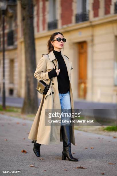 Heart Evangelista wears sunglasses from Dior, a black wool turtleneck pullover / sweater, a beige long trench coat from Dior, pale blue denim jeans /...