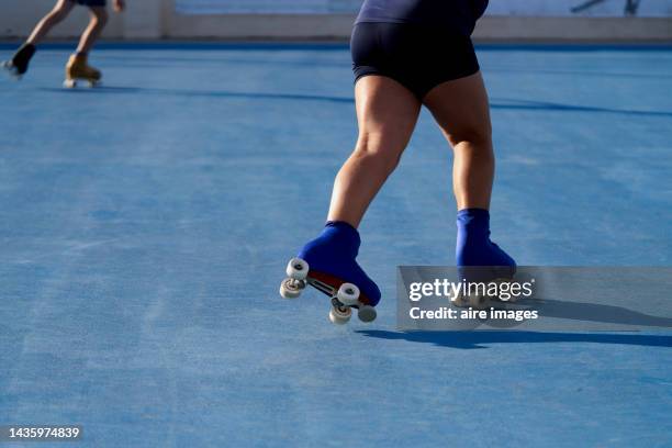 thick-legged girl dressed in black shorts riding on four-wheeled skates with protector training on the rink with her teammates - running shorts foto e immagini stock