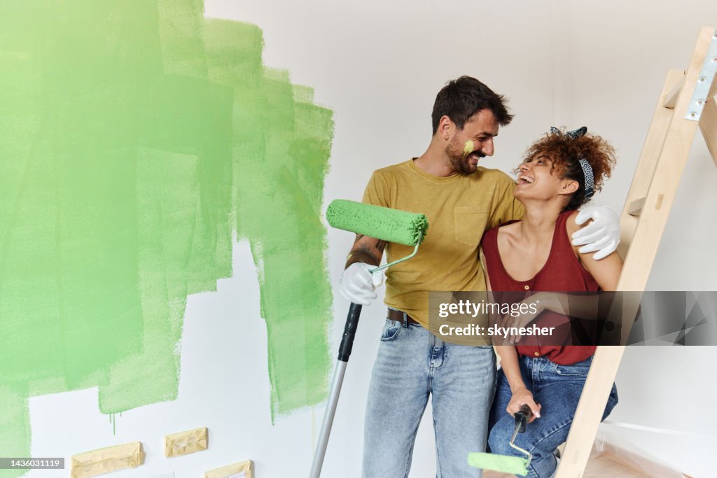 Coppia felice che parla mentre dipinge il loro nuovo appartamento.