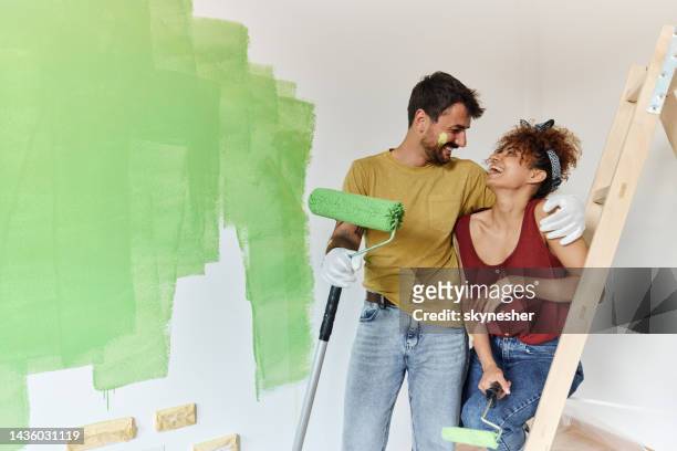 casal feliz conversando enquanto pinta seu novo apartamento. - renovação de casa - fotografias e filmes do acervo
