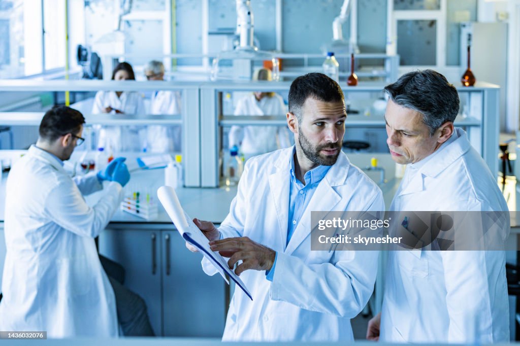 中年成人男性化学者は、実験室で科学研究に取り組んでいる間に話しています。