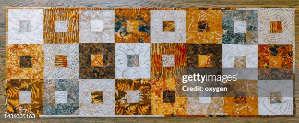 patchwork table runner with square block quilt. patchwork on autumn colors: orange, brown batiks fabrics on wooden table background. flat lay - table runner stock pictures, royalty-free photos & images