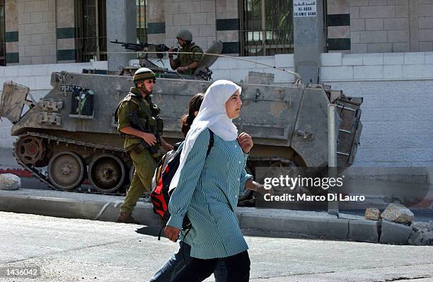 Palestinian schoolgirls walk past an Israeli armored vehicle and Israeli soldiers on patrol September 28, 2002 in the West Bank town of Ramallah....