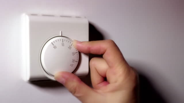 실내 온도 조절기를 사용하여 열을 낮추어 경제화. 여성의 손.