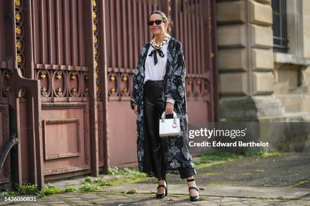 Alba Garavito Torre wears black sunglasses from Ray Ban, gold large earrings, a white latte large pearls necklace, a white silk shirt, a black with...