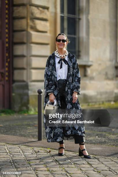 Alba Garavito Torre wears black sunglasses from Ray Ban, gold large earrings, a white latte large pearls necklace, a white silk shirt, a black with...