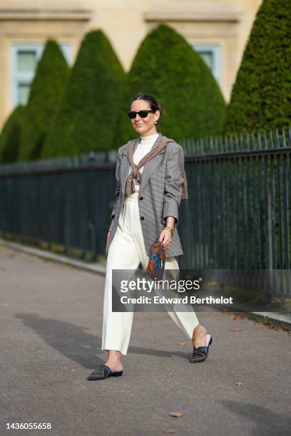 Alba Garavito Torre wears black sunglasses from Ray Ban, gold / black / white earrings, a white latte ribbed wool high neck t-shirt, a brown wool...