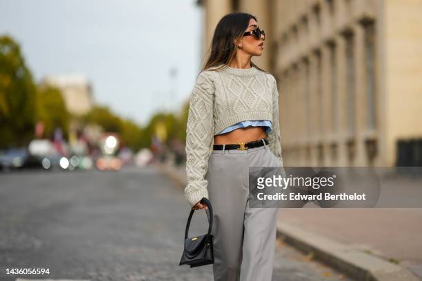 Angela Gonzalez wears black sunglasses from Celine, gold earrings, a pale gray embossed pattern cropped wool pullover, a pale blue cropped shirt, a...
