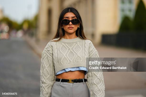 Angela Gonzalez wears black sunglasses from Celine, gold earrings, a pale gray embossed pattern cropped wool pullover, a pale blue cropped shirt, a...