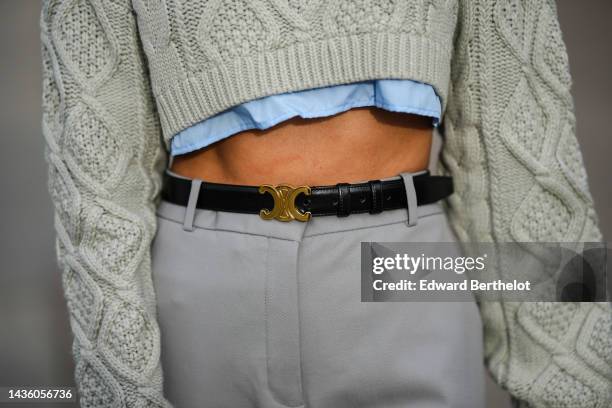 Angela Gonzalez wears a pale gray embossed pattern cropped wool pullover, a pale blue cropped shirt, a black shiny leather with gold logo buckle belt...