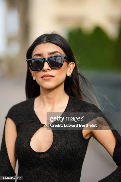 Angela Gonzalez wears black butterfly sunglasses, gold earrings, a black wool cut-out pattern wool body from Cider, black flared suit pants, gold...