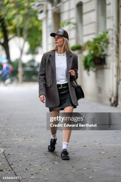 Natalia Verza wears a dark brown shiny leather snake print pattern cap, a white t-shirt, a pearls necklace, a brown wool oversized blazer jacket, a...