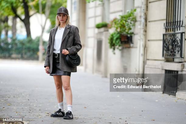 Natalia Verza wears a dark brown shiny leather snake print pattern cap, a white t-shirt, a pearls necklace, a brown wool oversized blazer jacket, a...