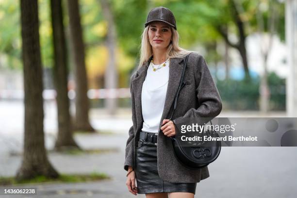 Natalia Verza wears a dark brown shiny leather snake print pattern cap, a white t-shirt, a pearls necklace, a brown wool oversized blazer jacket, a...