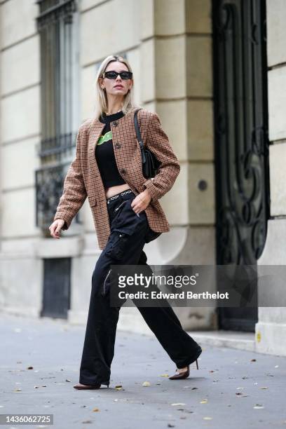 Natalia Verza wears black sunglasses from Miu Miu, silver earrings, a pearls necklace, a black with yellow and green painted pattern cropped t-shirt,...