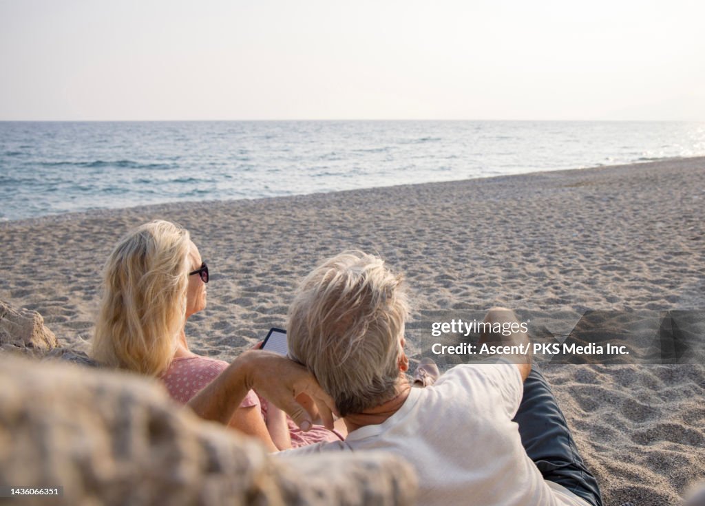 Mature couple relax on beach, using e-reader