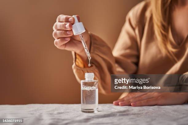 a girl in a beige dress holds a pipette with a drop of serum in her hands. - serum sample stock pictures, royalty-free photos & images
