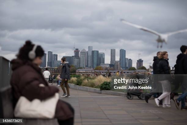 General view of Canary Wharf as people sit and walk by the bank of the River Thames on an overcast day in Greenwich on October 23, 2022 in London,...