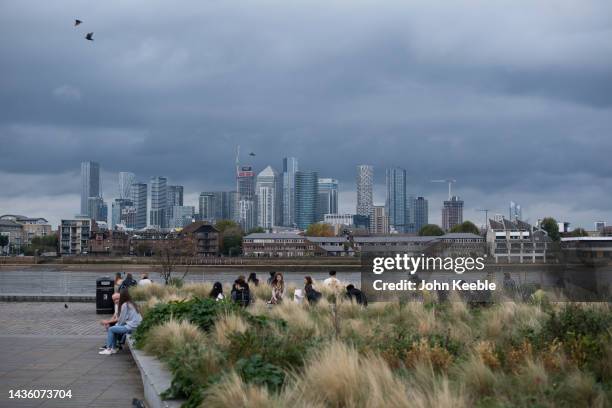 General view of Canary Wharf as people sit by the bank of the River Thames on an overcast day in Greenwich on October 23, 2022 in London, England.