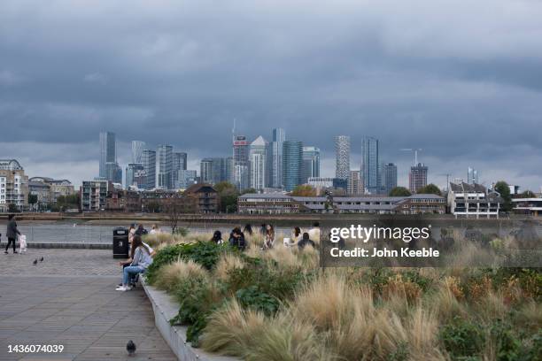 General view of Canary Wharf as people sit by the bank of the River Thames on an overcast day in Greenwich on October 23, 2022 in London, England.