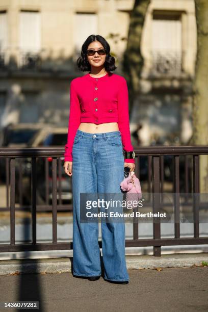 Guest wears black sunglasses, a neon pink and red buttoned wool cropped cardigan, pale blue denim wide legs pants, a black shiny leather with...