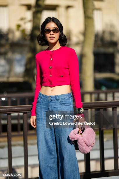 Guest wears black sunglasses, a neon pink and red buttoned wool cropped cardigan, pale blue denim wide legs pants, a black shiny leather with...