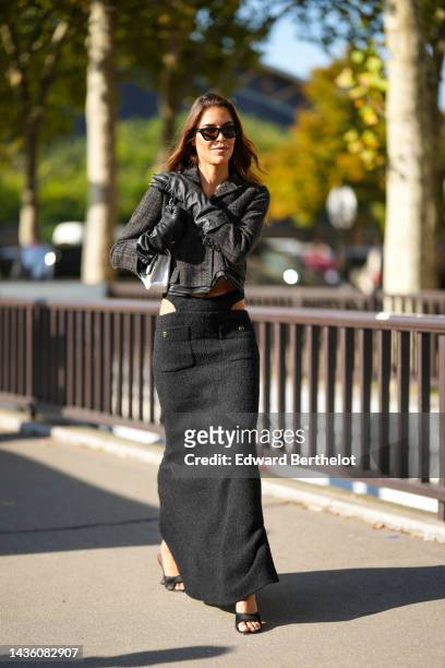 Guest wears black square sunglasses, a black checkered print pattern wool buttoned jacket, a black wool cut-out waist / slit long skirt from Chanel,...