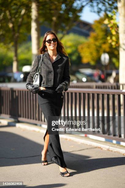 Guest wears black square sunglasses, a black checkered print pattern wool buttoned jacket, a black wool cut-out waist / slit long skirt from Chanel,...