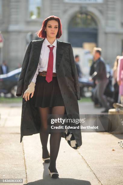 Guest wears black cat eyes sunglasses, silver earrings, a white shirt, a red with gray print pattern silk tie from Laurent Perrier, a black long silk...