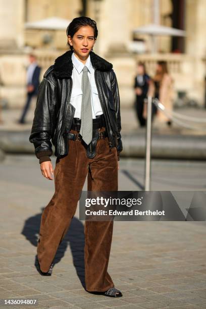 Guest wears a black shiny leather jacket with a black fluffy collar, a white shirt, a gray tie, a black shiny leather belt, brown ribbed velvet large...