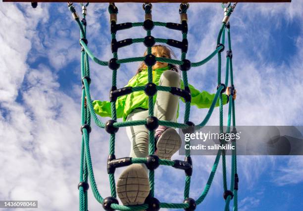 elementary school aged little girl climbing on the rope climbing web stair at playground - extreem weer stock pictures, royalty-free photos & images