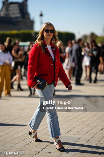 Guest wears black sunglasses, a white t-shirt, a red wool with black borders buttoned jacket , pale blue faded denim flared pants, a black shiny...