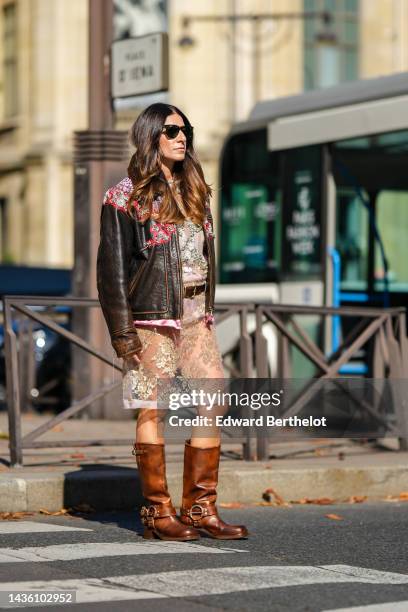 Guest wears black sunglasses from Ray Ban, a dark brown shiny leather with embroidered red leather / silver and pink crystal print pattern zipper...