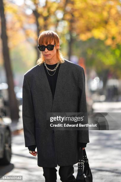 Guest wears black sunglasses from Celine, silver large chain necklaces, a black t-shirt, a dark gray oversized blazer jacket, a black shiny leather...